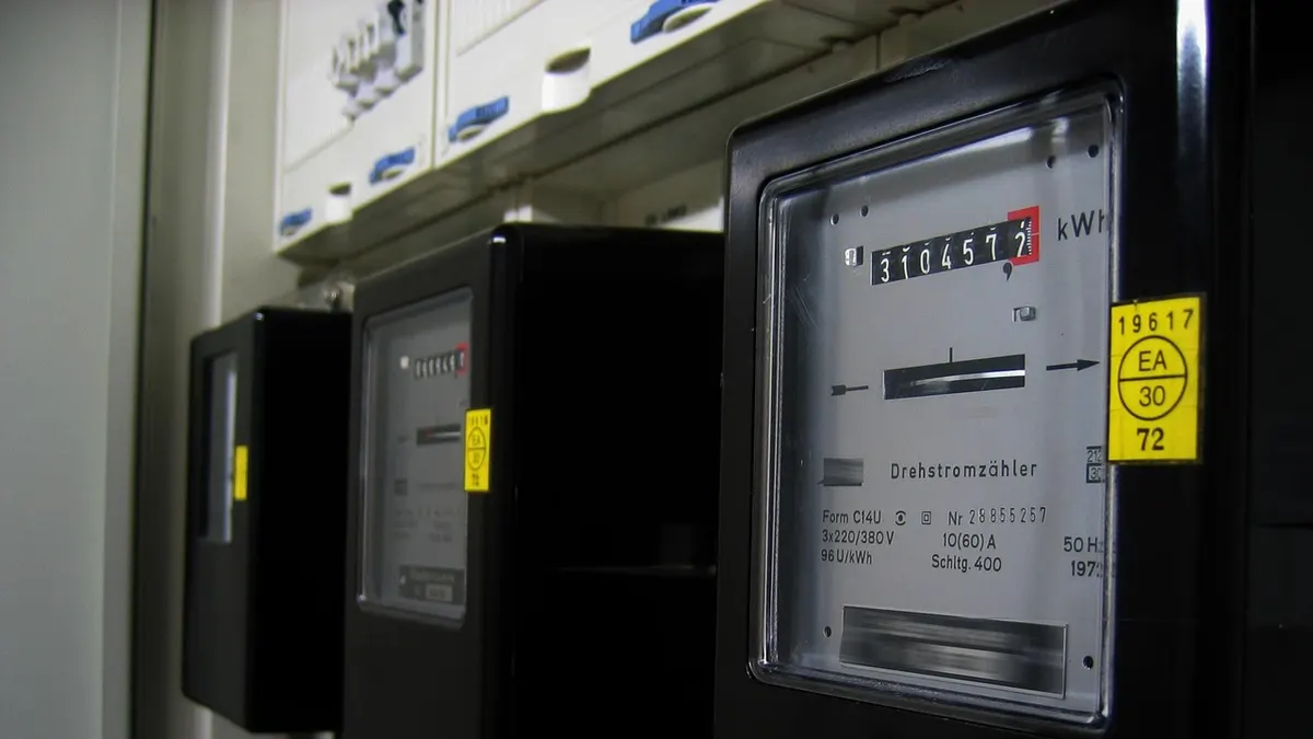 Três medidores de energia elétrica analógicos pretos em fila na parede
