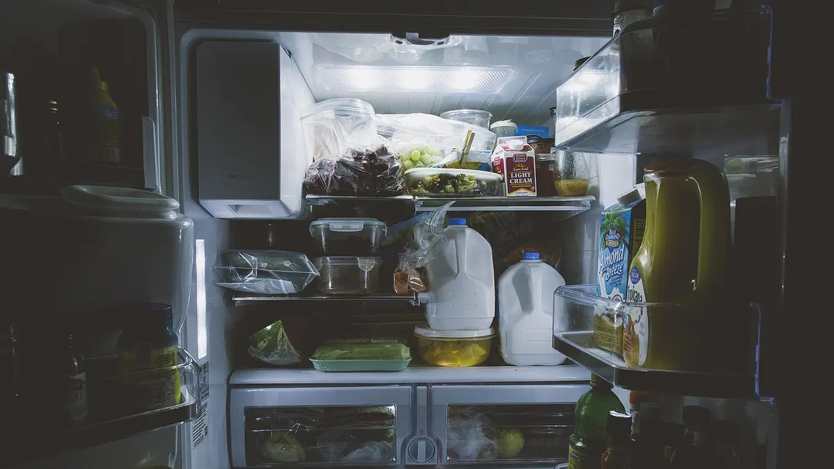 Geladeira aberta e iluminada com galões de leite e alimentos